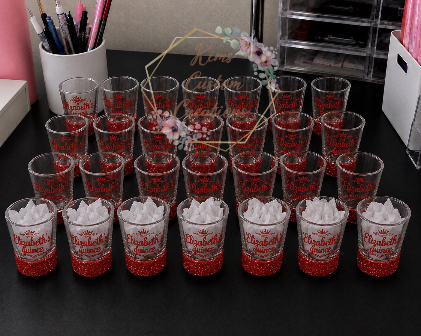 Personalized quinceanera shot glasses with red glitter bases arranged for a quince toast