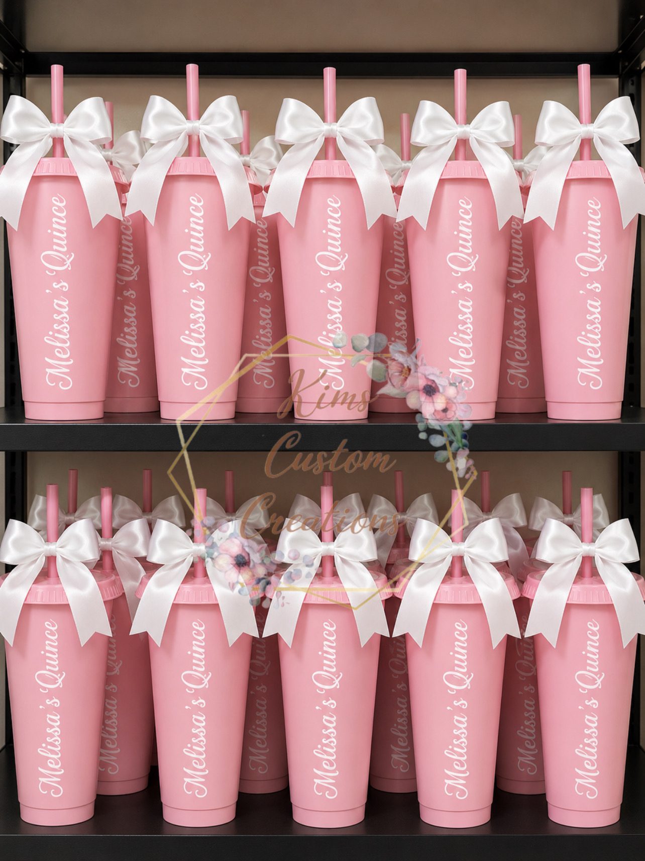 Pink personalized quinceanera tumblers with lids, straws, and white satin bows lined up on shelves